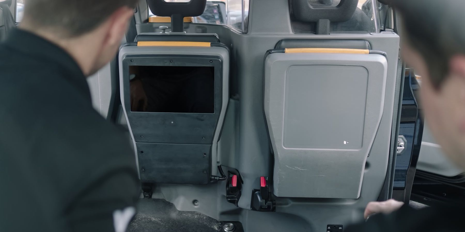 Two Orison fitters working at the open seat-back aperture inside a black cab, mid-installation.